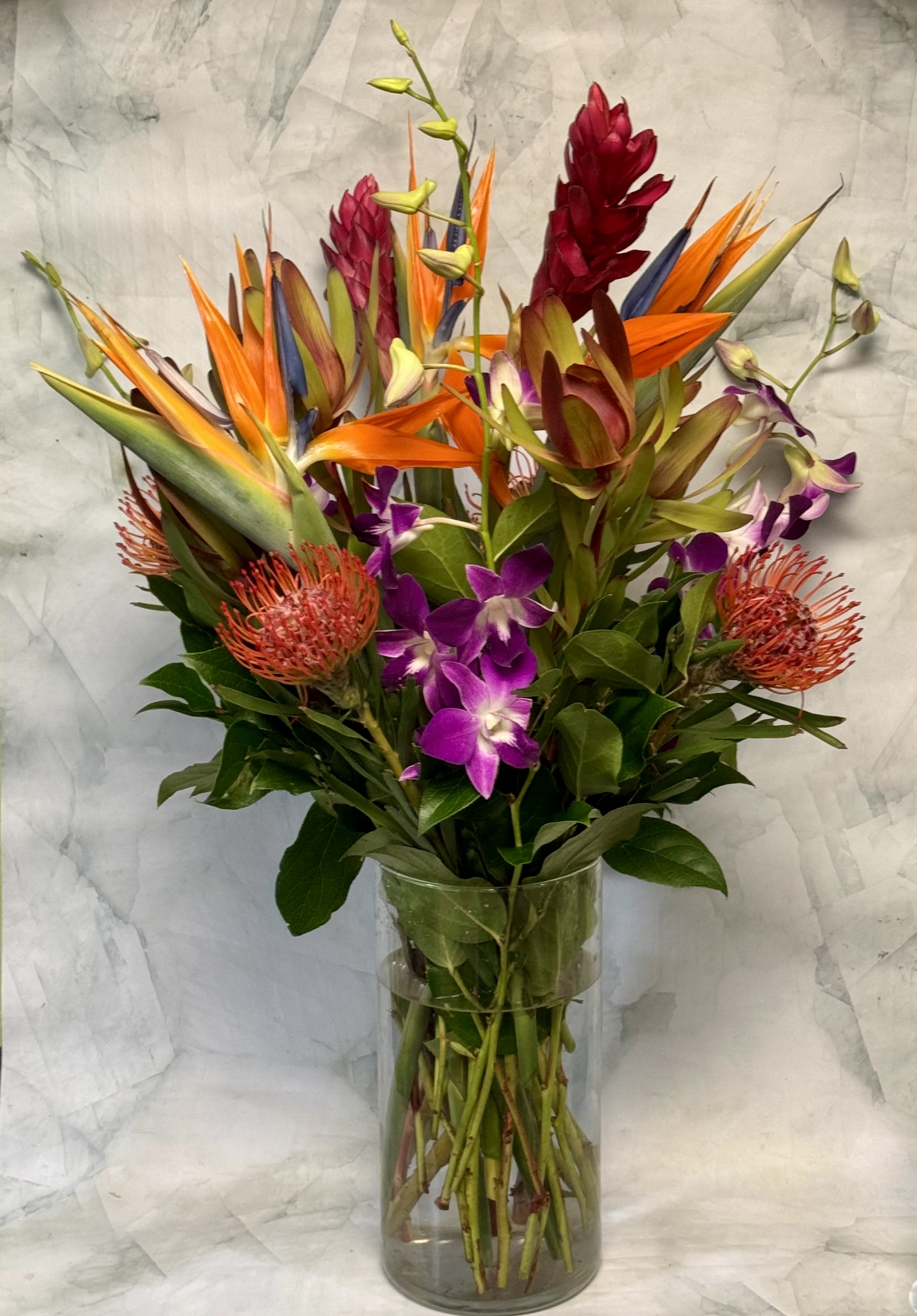 Tropical bouquet with orange bird-of-paradise and purple orchids in a glass vase