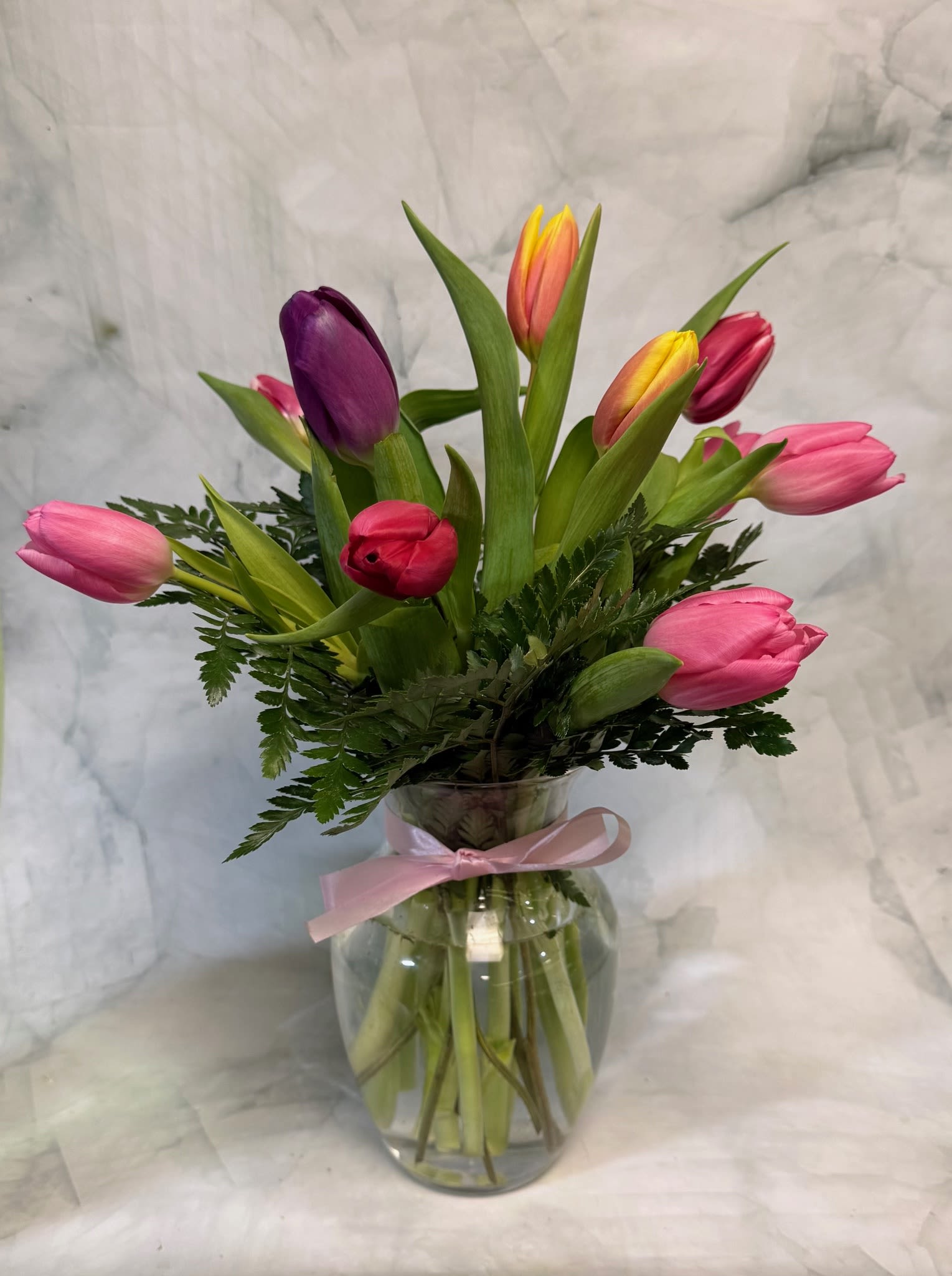 Mixed tulips in a clear glass vase with a pink ribbon