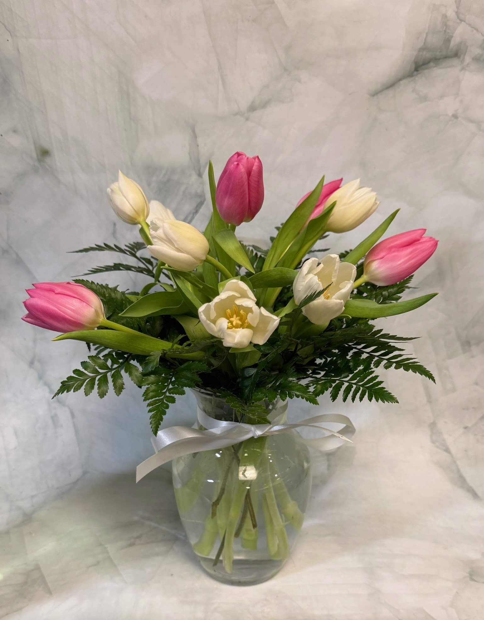Pink and white tulips in a glass vase with a white ribbon