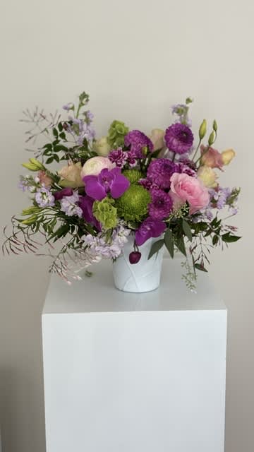 Mixed pink, purple, and green flowers arranged in a white vase