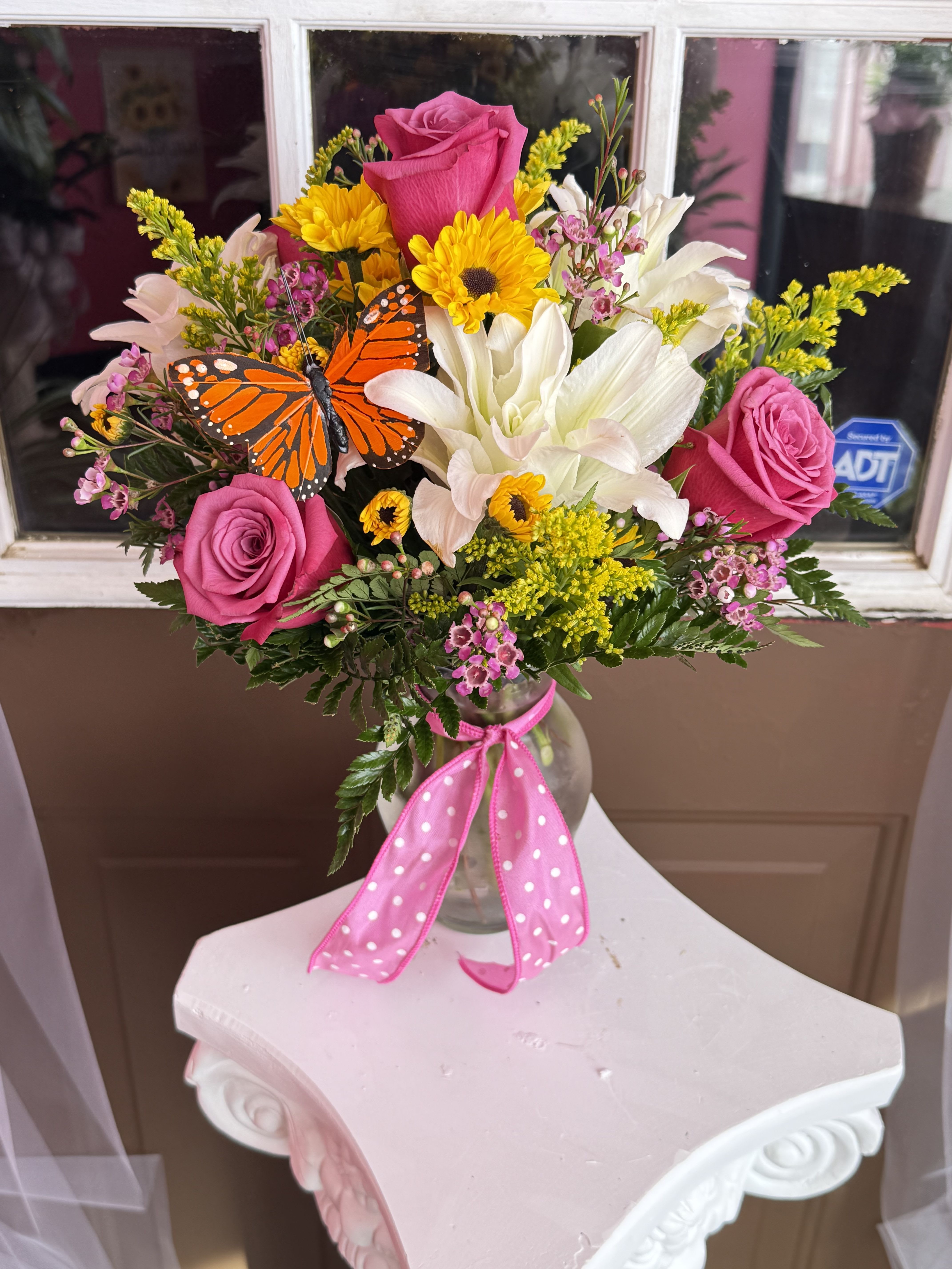 Pink roses and white lilies in a glass vase with a butterfly accent