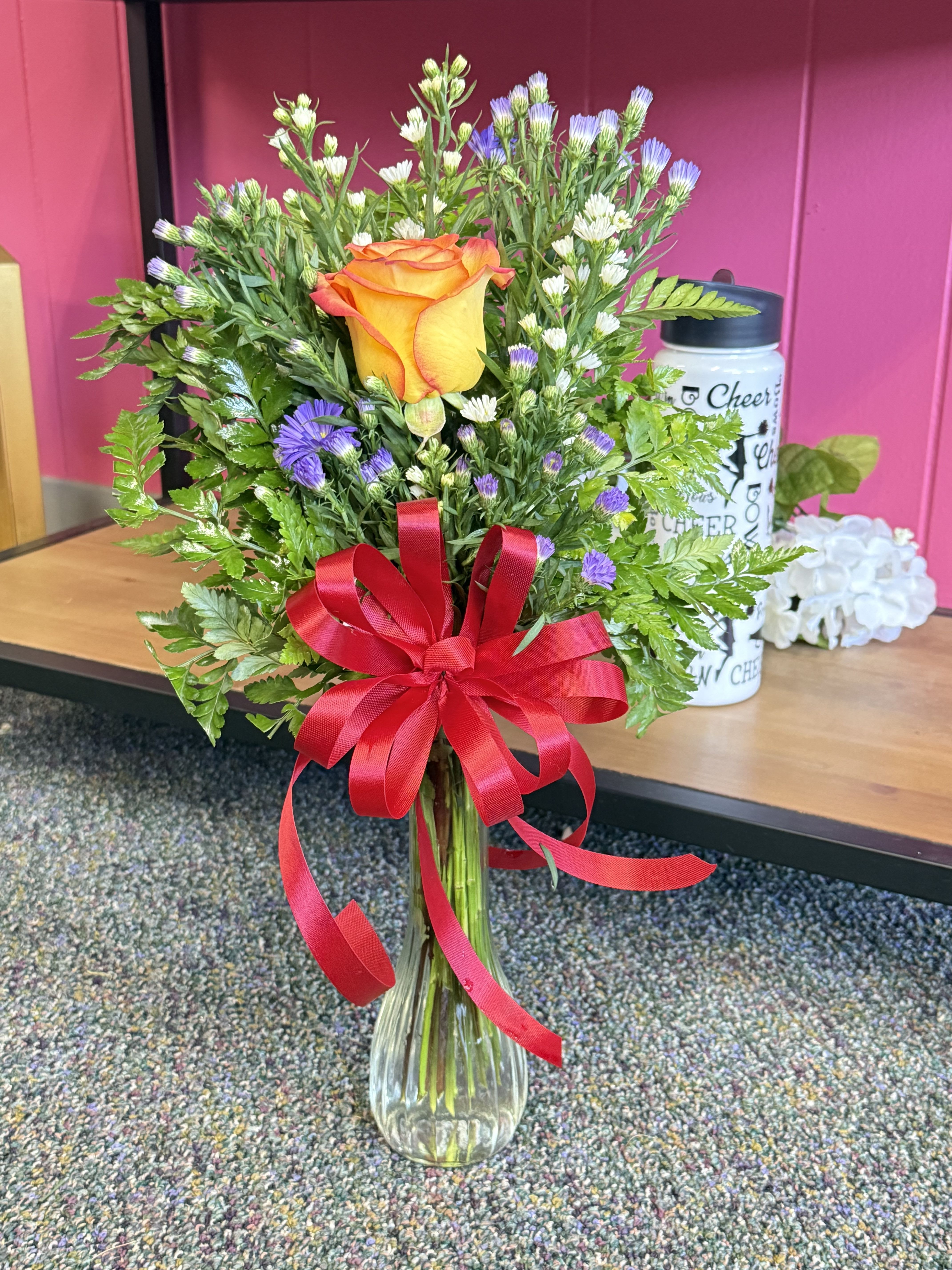 Orange rose bouquet in a clear glass vase with a red ribbon