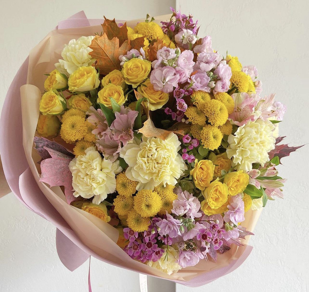 Bouquet of yellow, pink, and cream flowers wrapped in blush paper