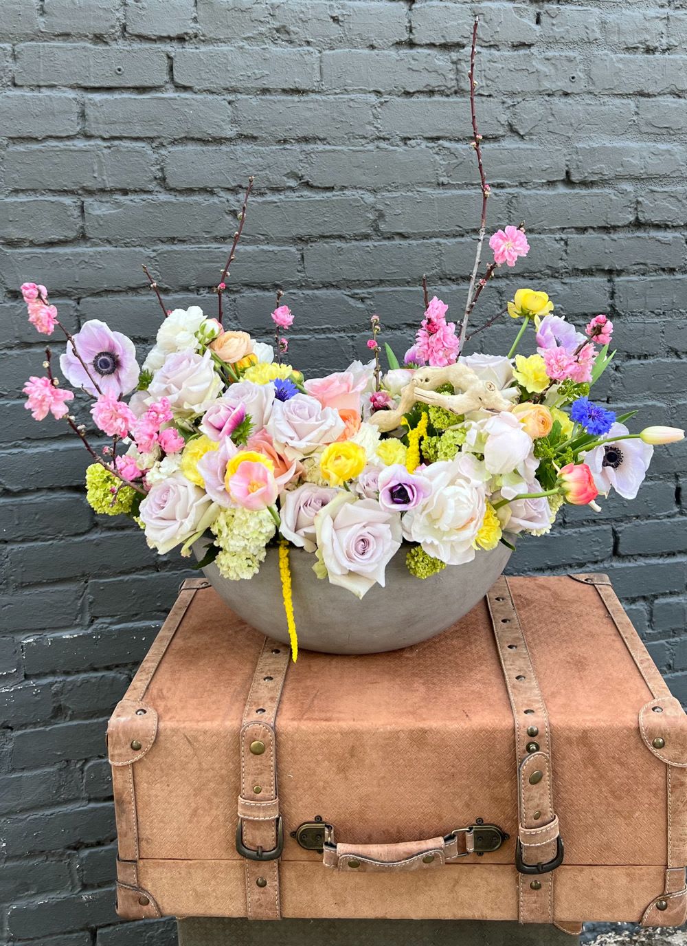 Mixed pastel flower arrangement in a shallow bowl on a vintage suitcase