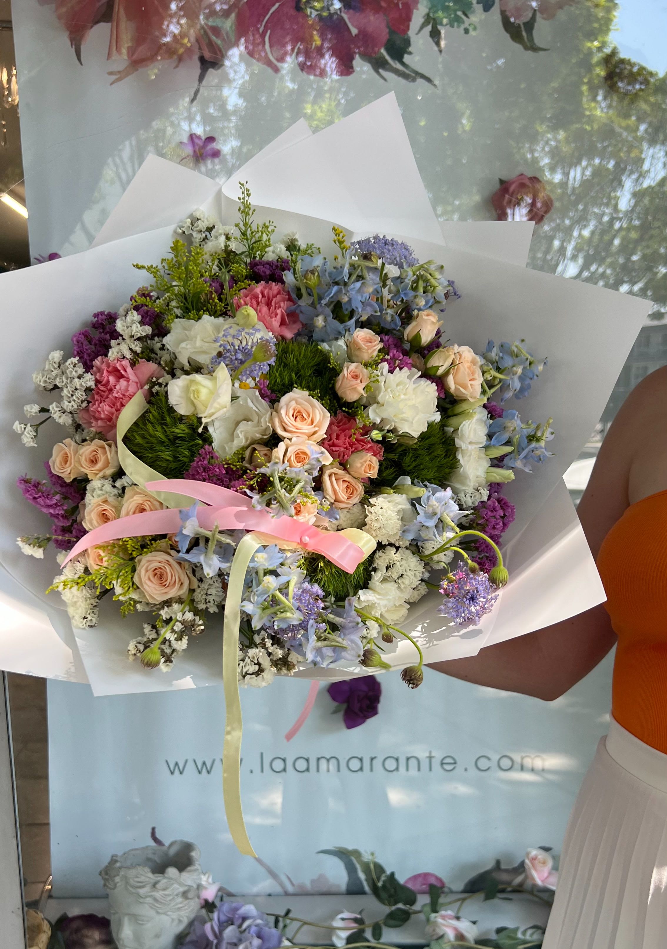 Mixed bouquet of pastel roses, carnations, and blue flowers wrapped in white paper