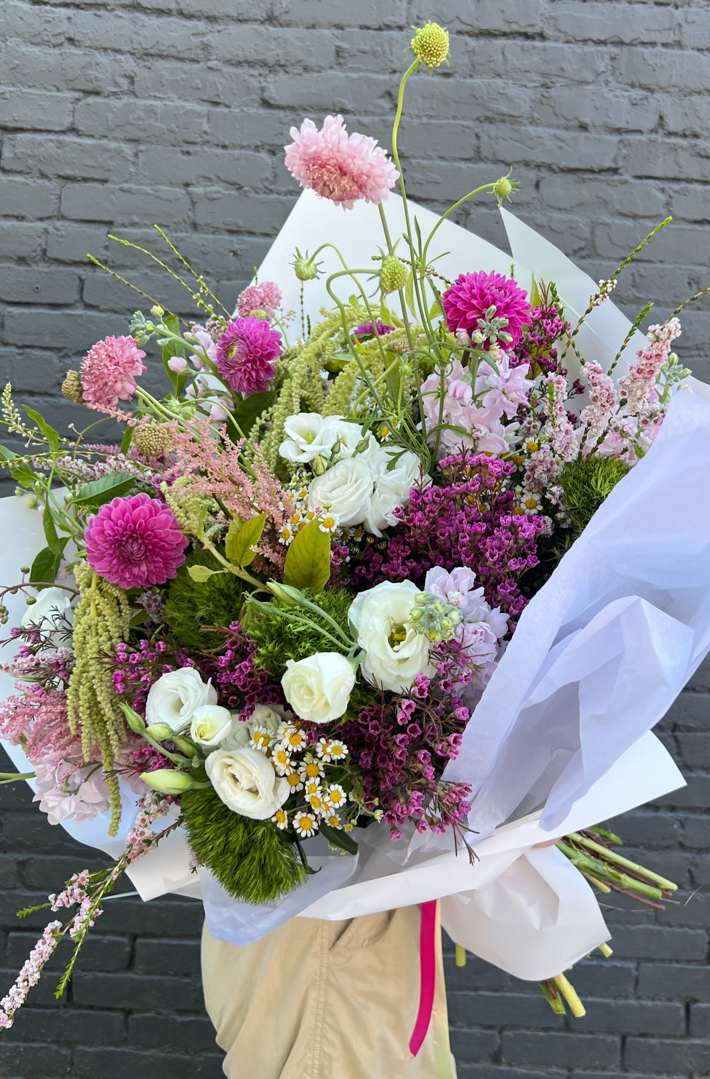 Hand-tied bouquet of pink, white, and purple flowers wrapped in white paper