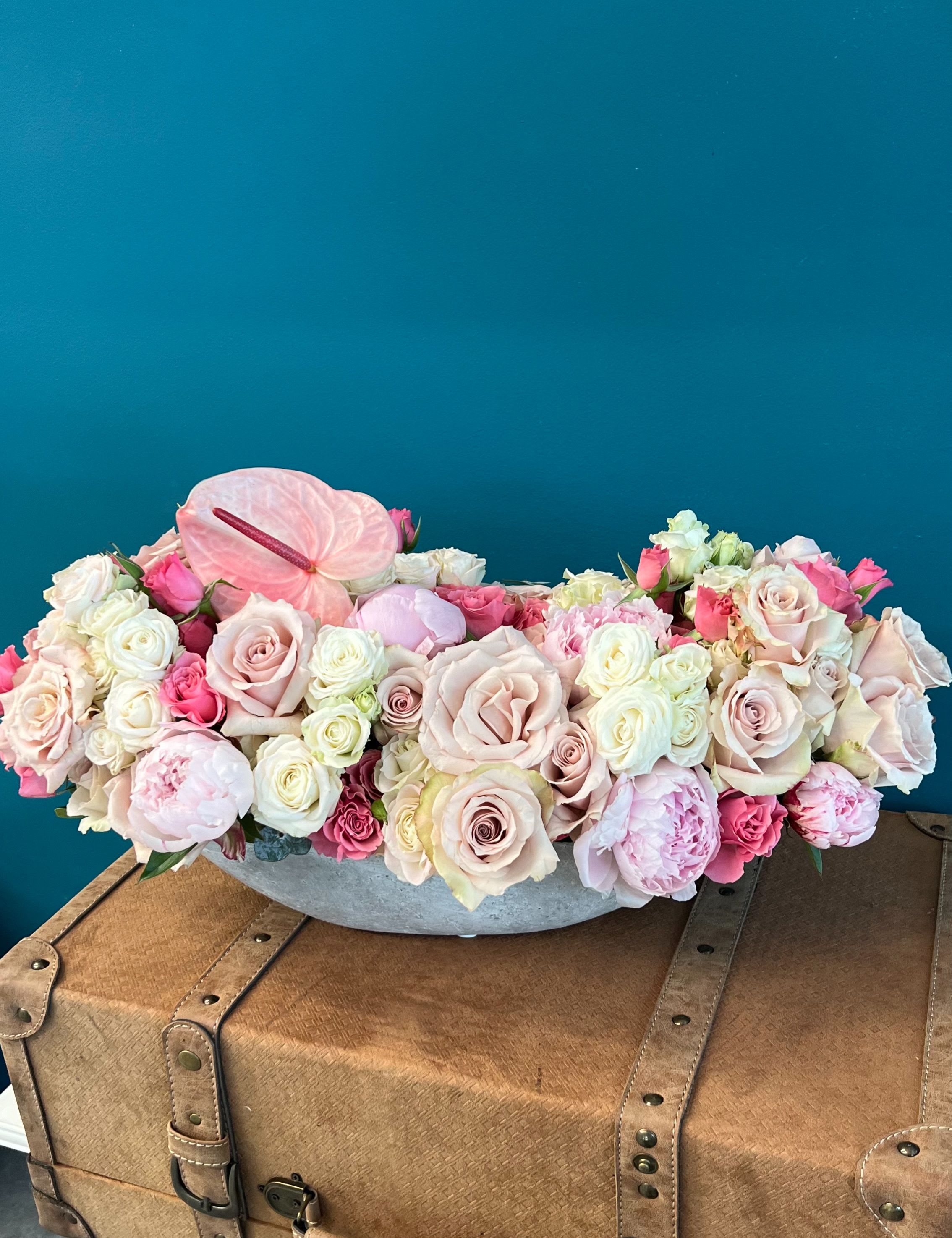 Low floral arrangement of pale pink and white roses with anthurium in a gray container