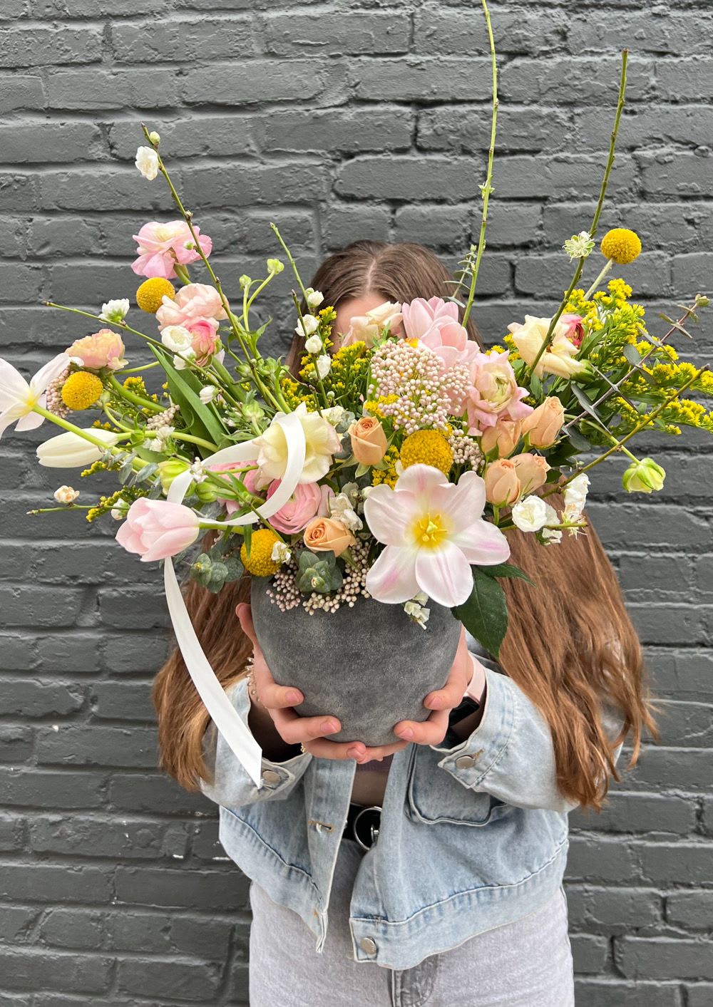 Large pastel flower arrangement in a gray vase held by a person