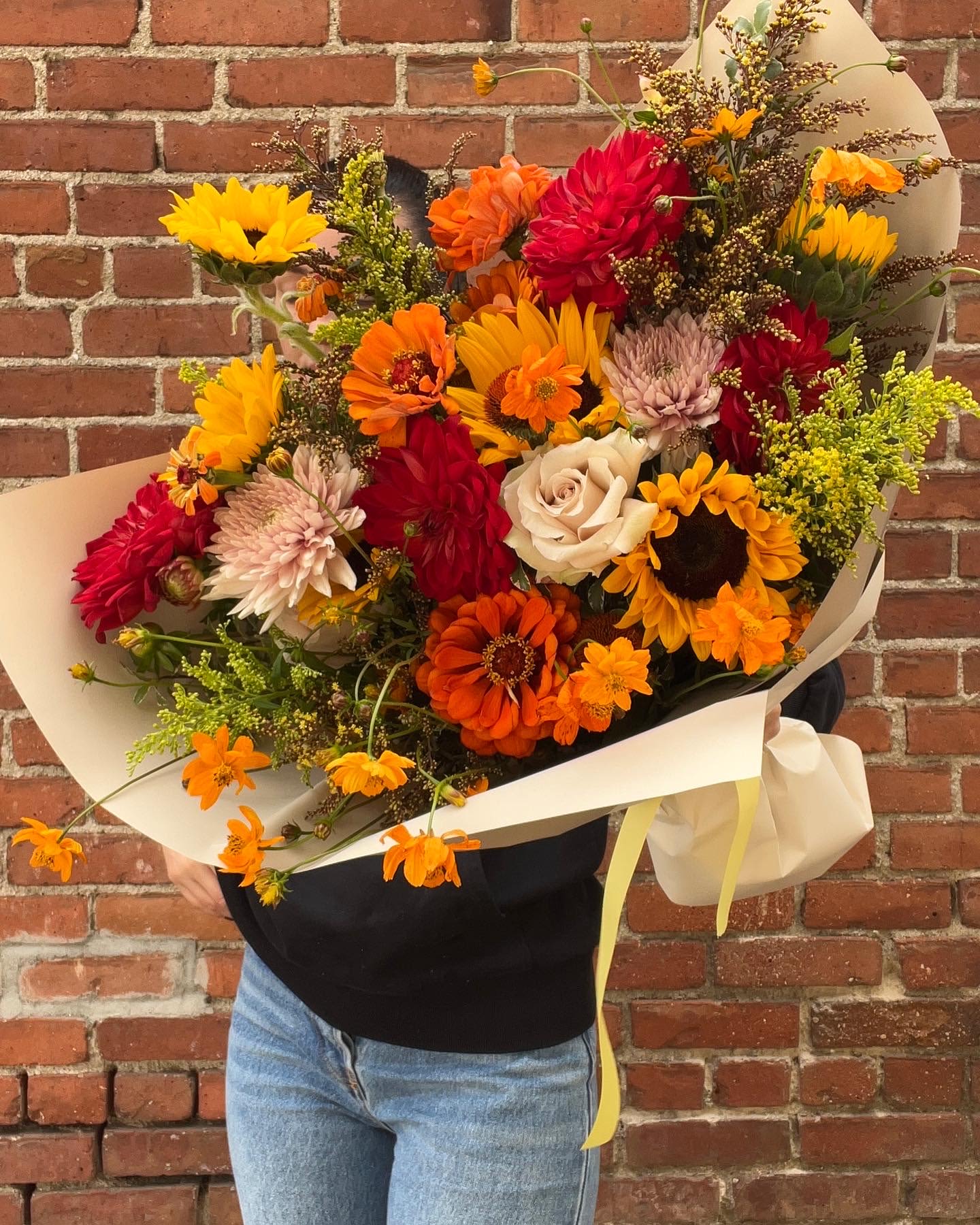 Large bouquet of sunflowers, dahlias, and roses wrapped in cream paper