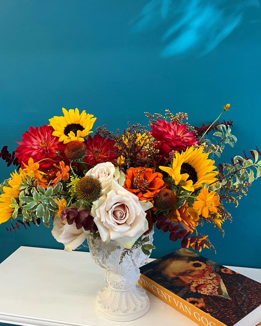 Colorful bouquet with sunflowers, roses, and orange blooms in a white vase