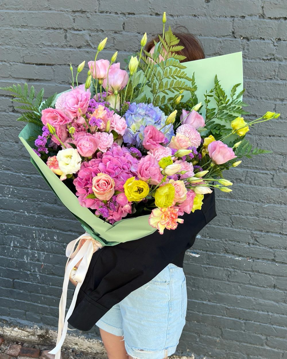 Large mixed bouquet of pink, purple, and yellow flowers wrapped in green paper