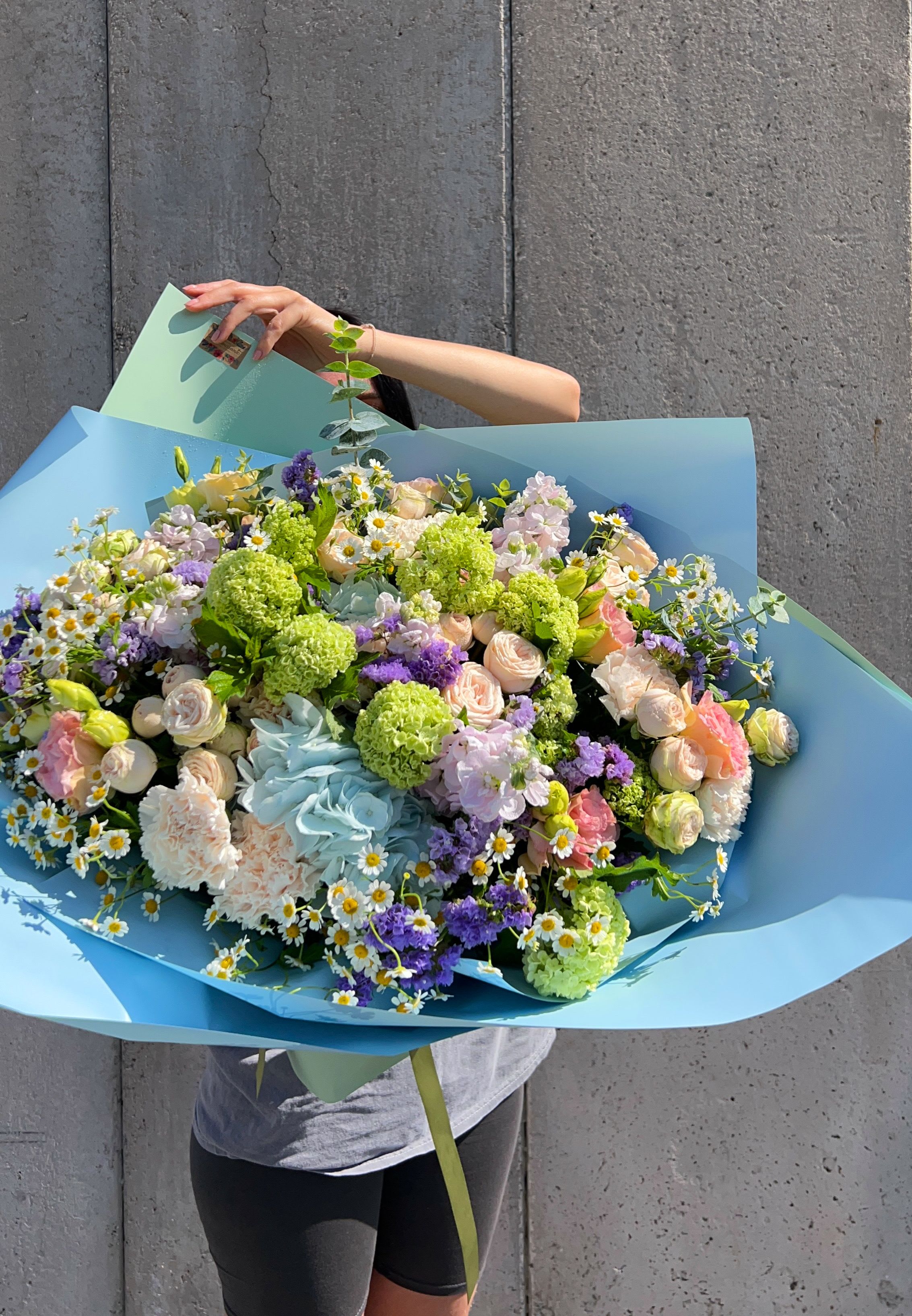 Large pastel bouquet with roses, carnations, and daisies wrapped in blue paper