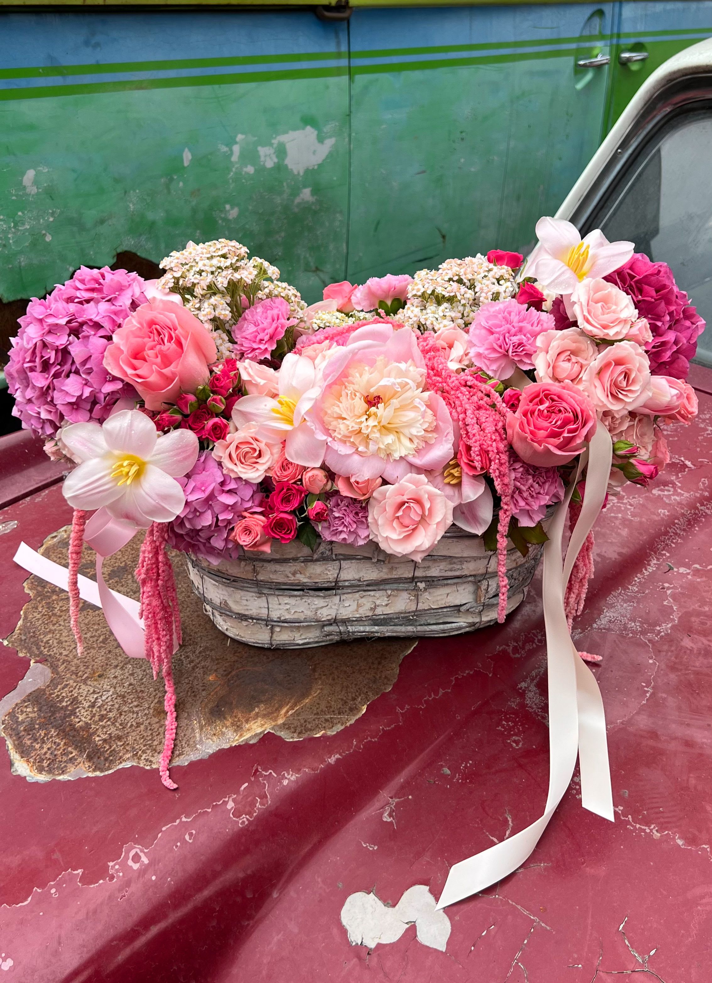 Pink floral arrangement in a woven basket with ribbon accents