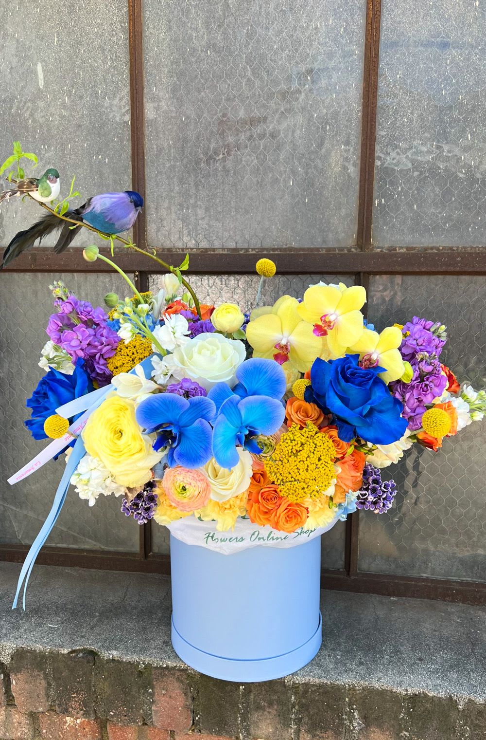 Bright mixed bouquet in a blue hatbox with a bird decoration