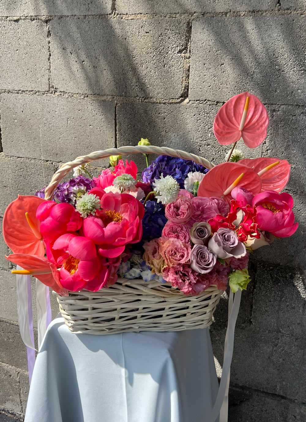 Basket arrangement with pink anthuriums, peonies, and roses