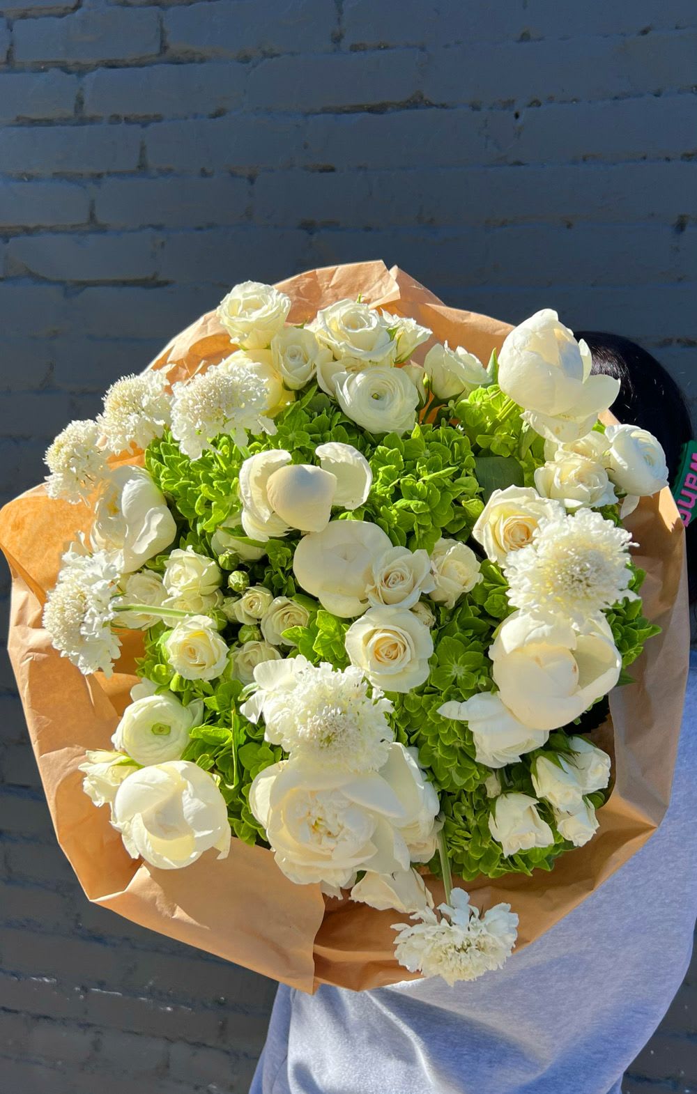 Bouquet of white flowers with bright green hydrangeas wrapped in tan paper