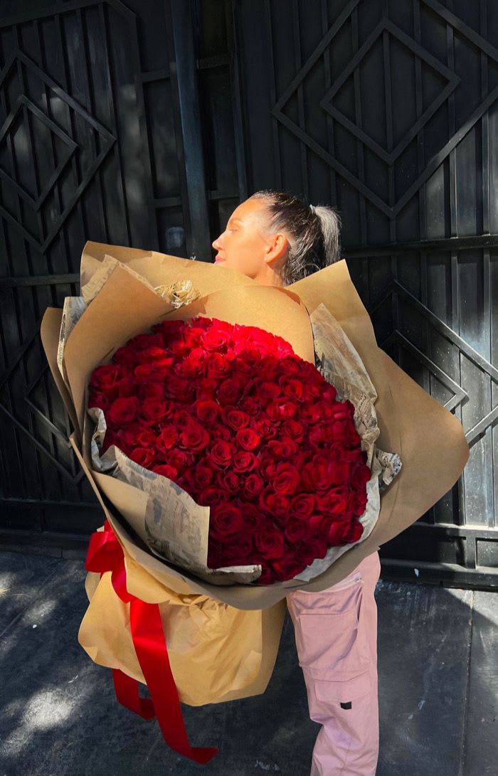 Woman holding a large bouquet of red roses wrapped in brown paper