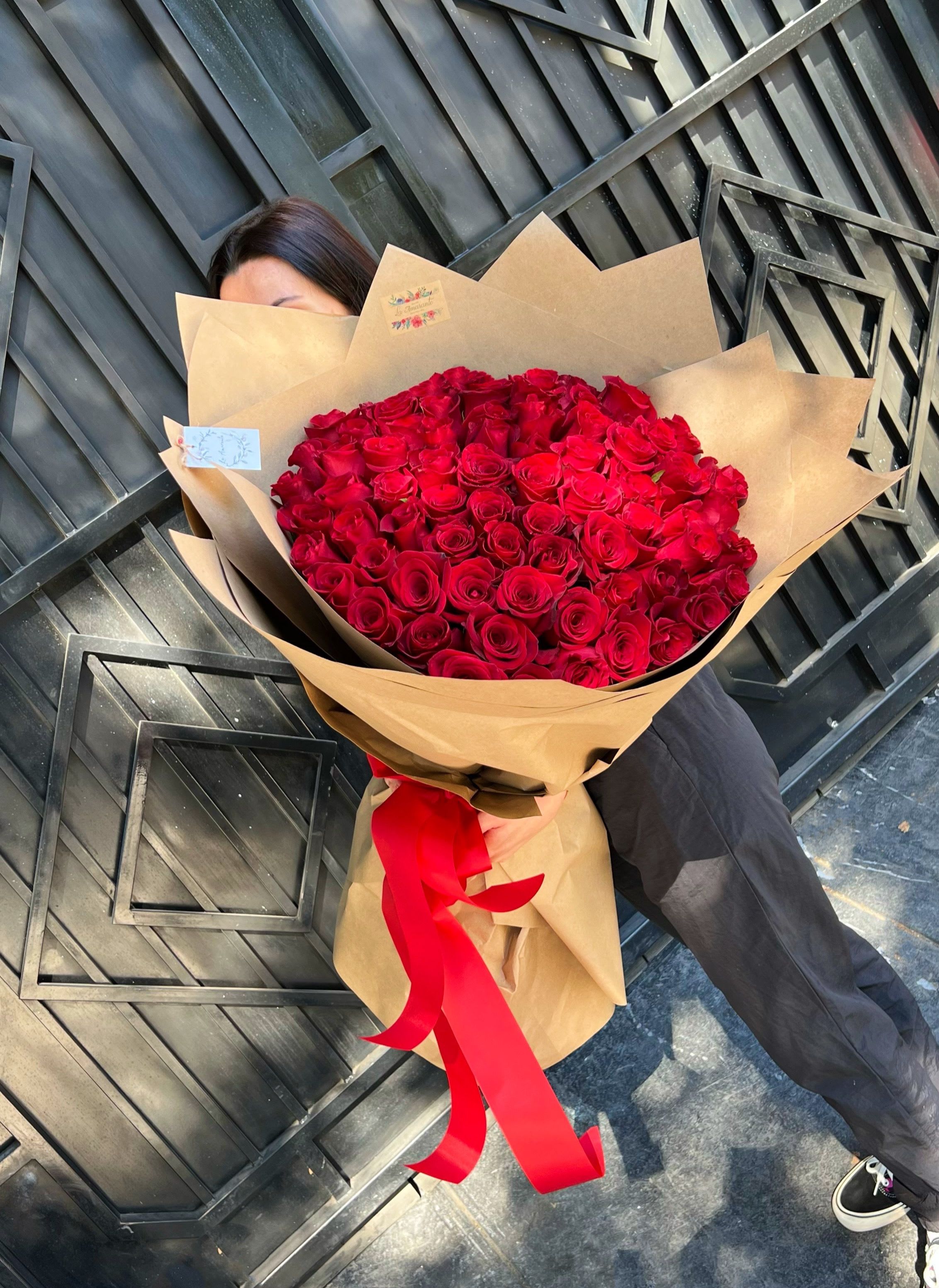 Large bouquet of red roses wrapped in brown paper with a red ribbon