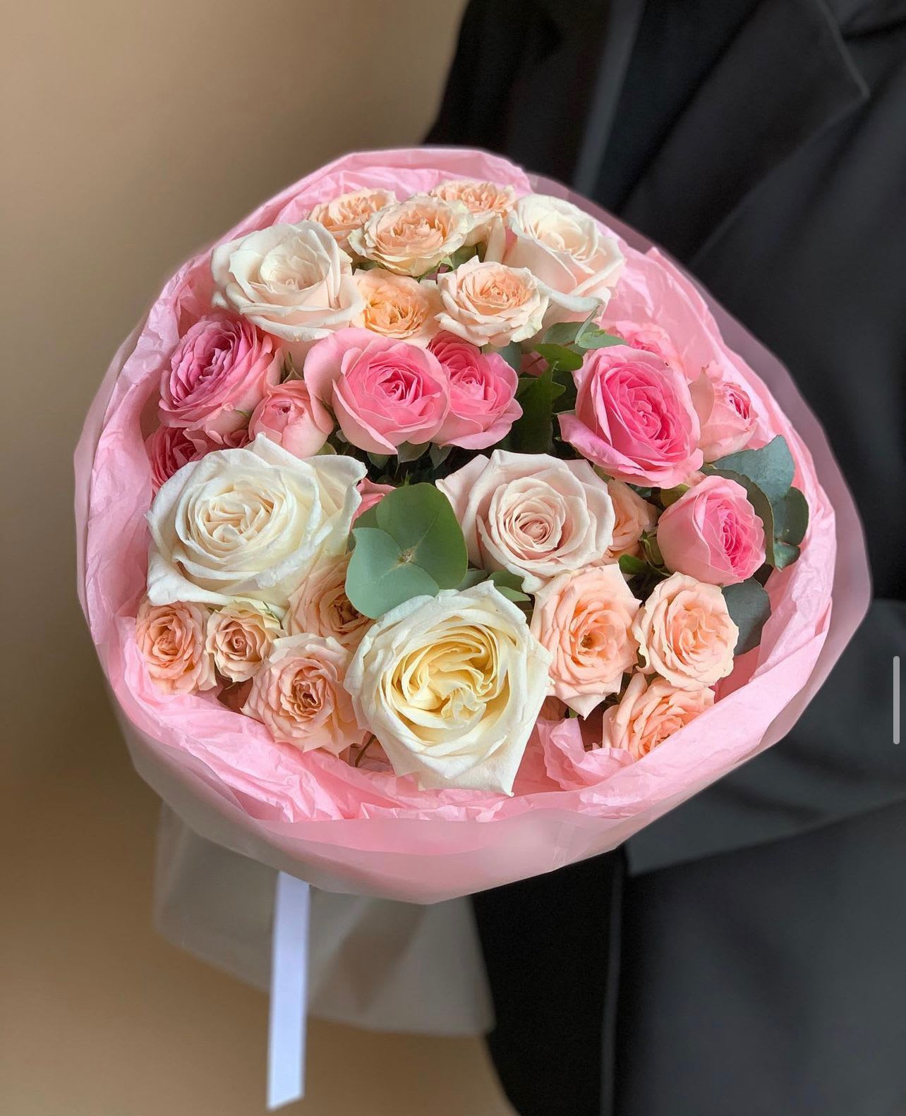 Bouquet of pink, peach, and white roses wrapped in pink paper