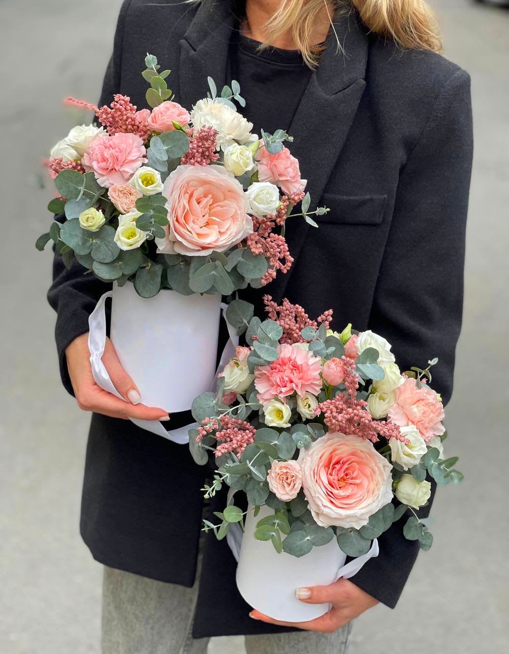 Two pastel flower arrangements in white hat boxes held by a person