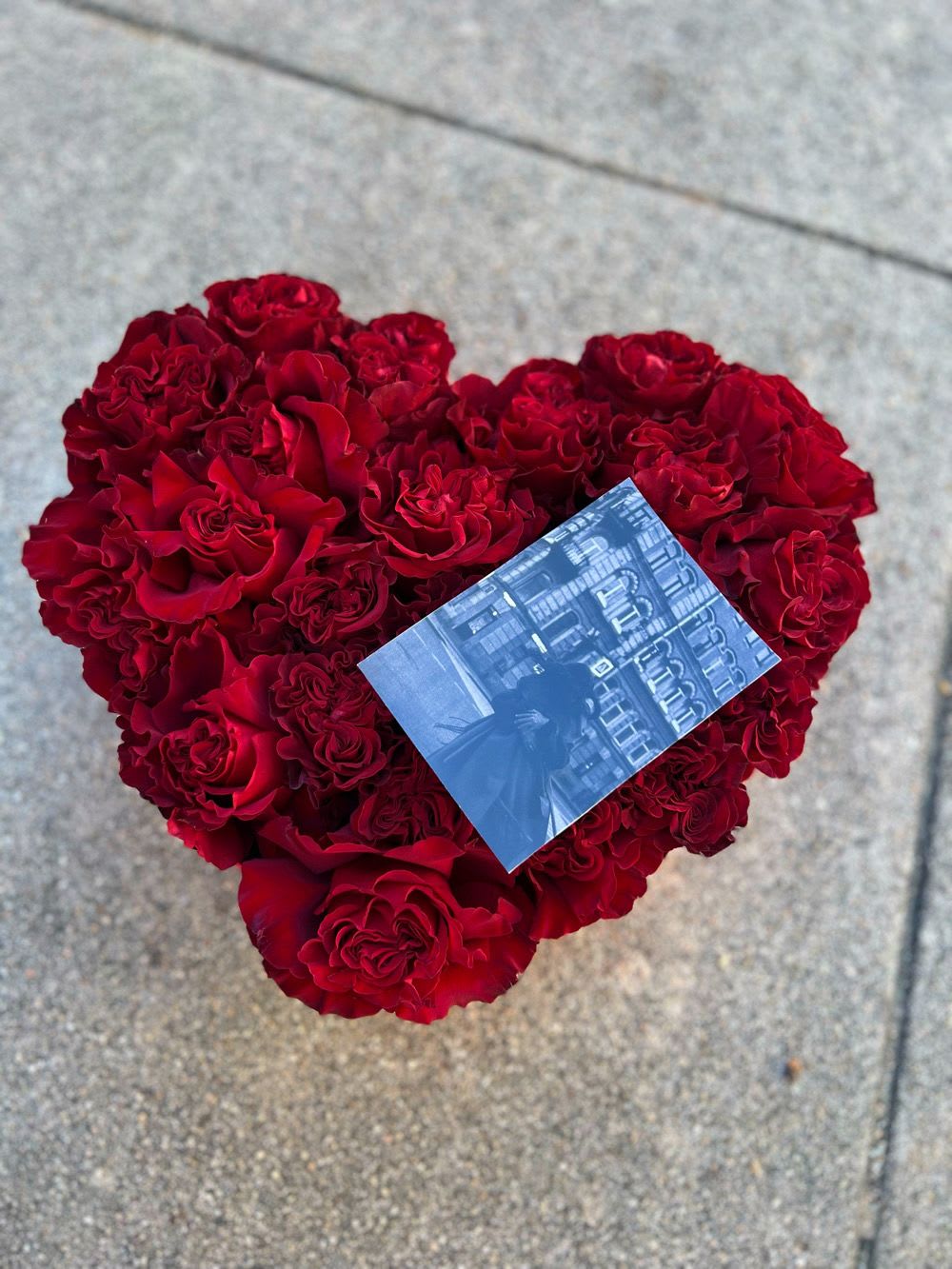 Heart-shaped bouquet of red roses with a small photo card on top