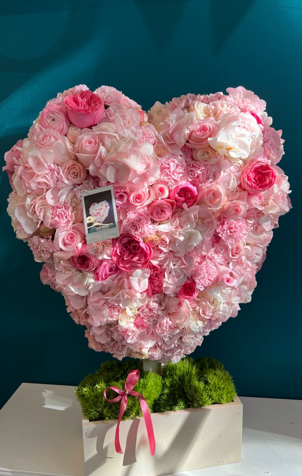 Heart-shaped pink floral arrangement in a box with a ribbon