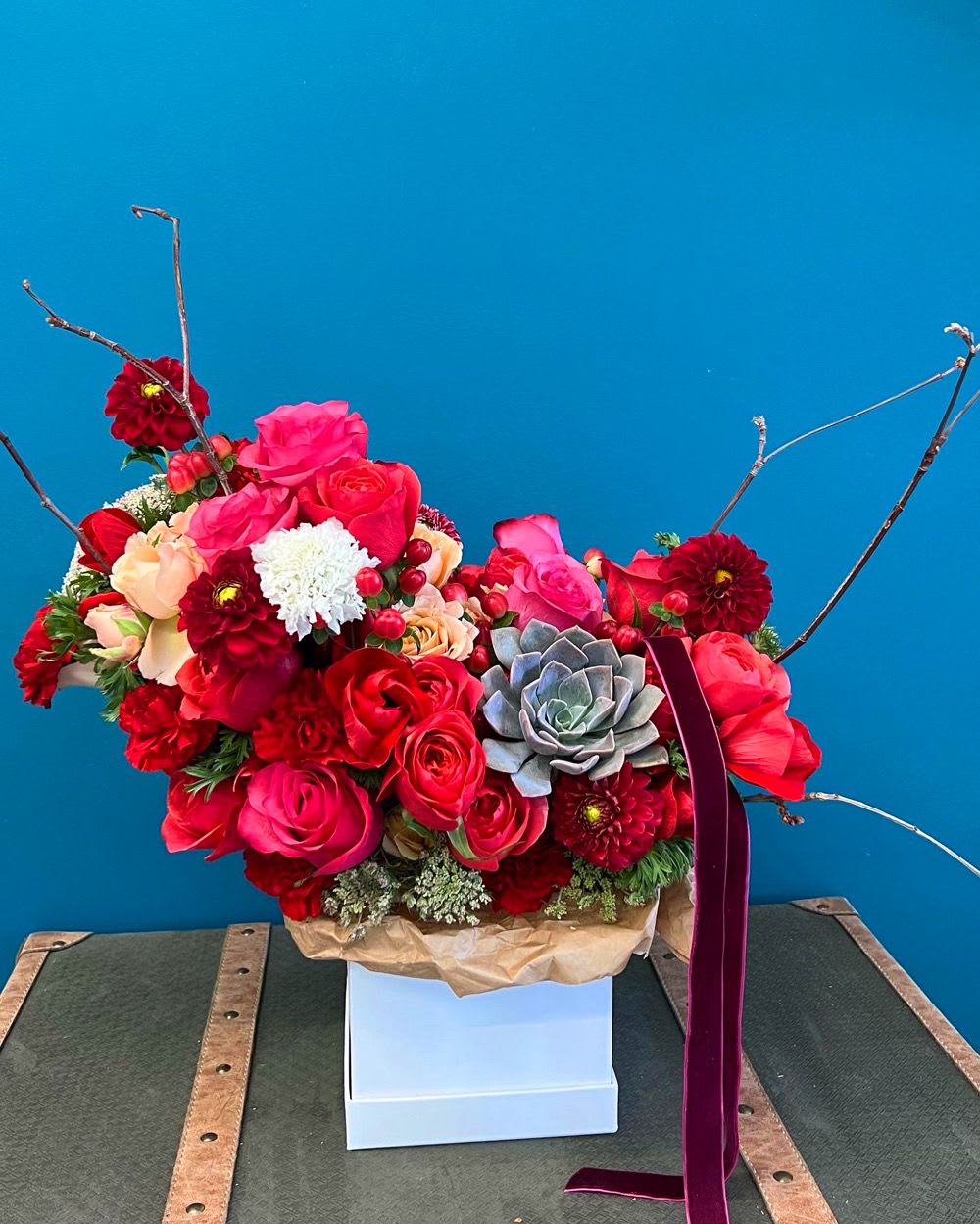 Bright red and pink floral arrangement with roses and a succulent in a white box