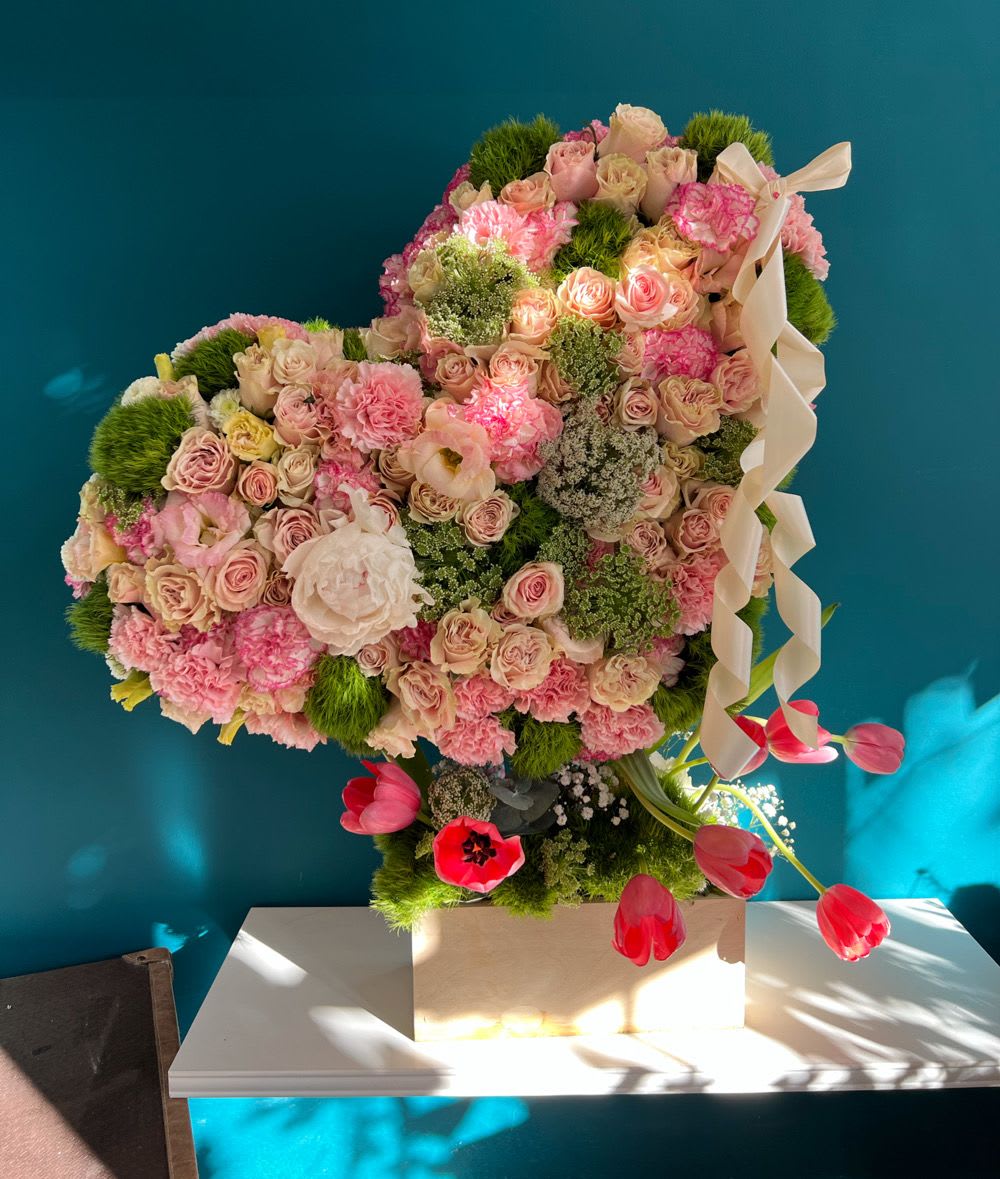 Heart-shaped floral arrangement with pink roses and carnations on a pedestal