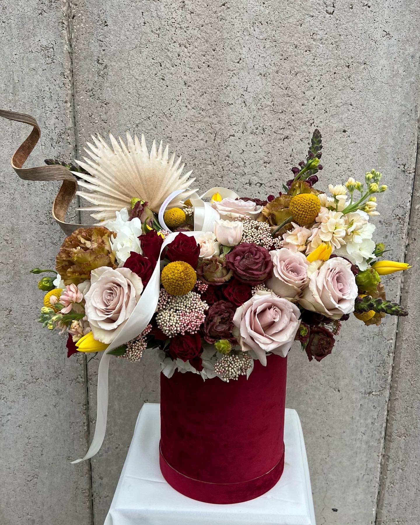 Mixed roses and small blooms in a burgundy hatbox with ribbon