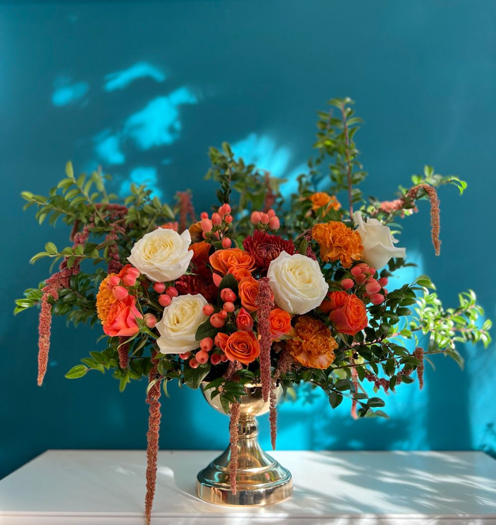 Mixed orange and white floral arrangement in a gold vase
