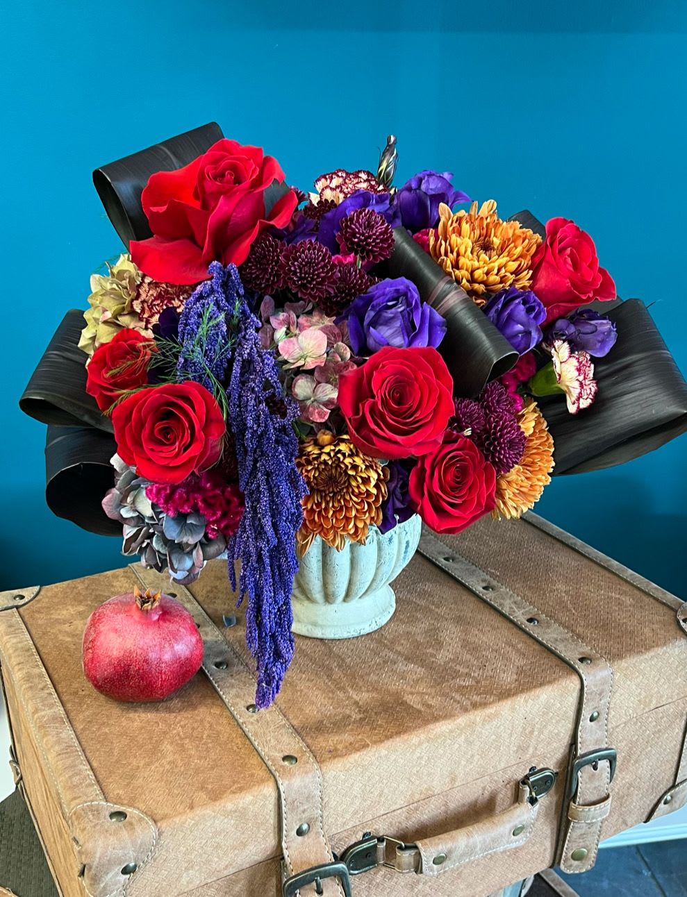 Bouquet of red roses, purple blooms, and orange chrysanthemums in a pale vase