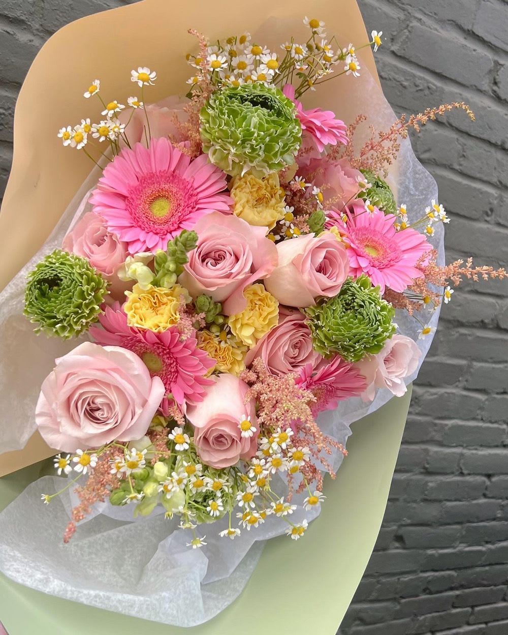 Bouquet of pink roses, gerbera daisies, and green blooms wrapped in paper