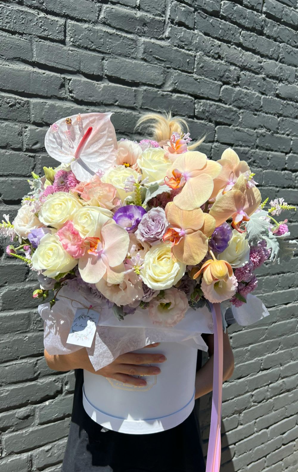 Pastel bouquet with orchids, roses, and a white anthurium in a round box