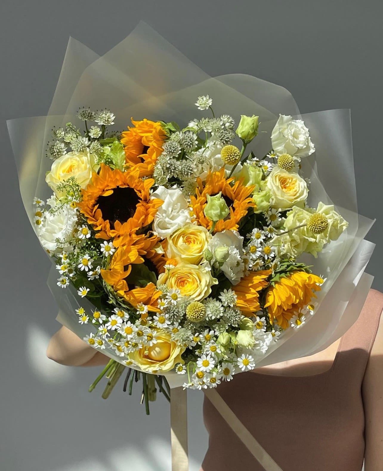 Bouquet of sunflowers, yellow roses, and white daisies wrapped in clear paper