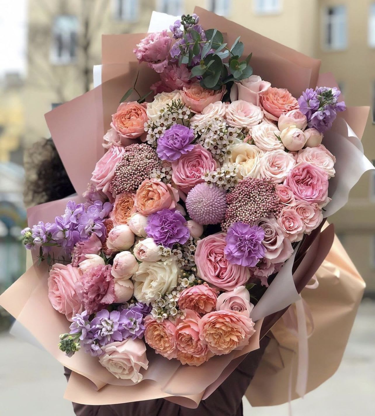 Large bouquet of pink, peach, and lavender flowers wrapped in blush paper