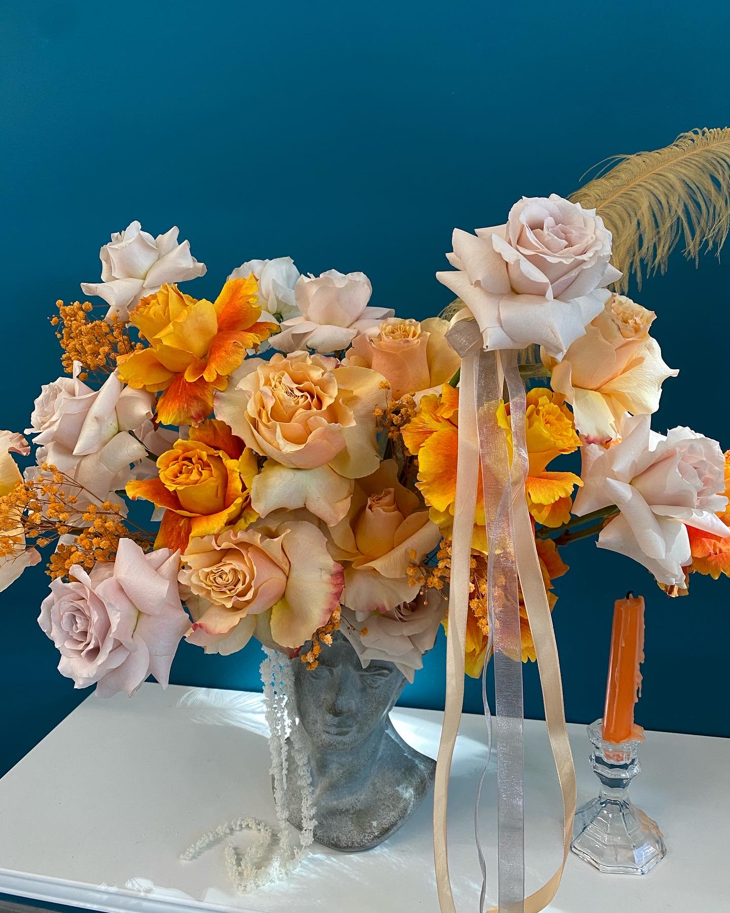 Peach and white roses with orange flowers in a bust vase