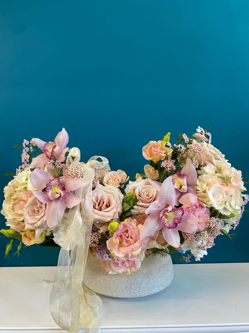 Pastel floral arrangement with orchids and roses in a low white vase