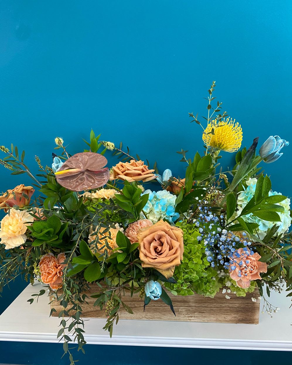 Mixed floral arrangement in a wooden box with peach roses and blue hydrangeas