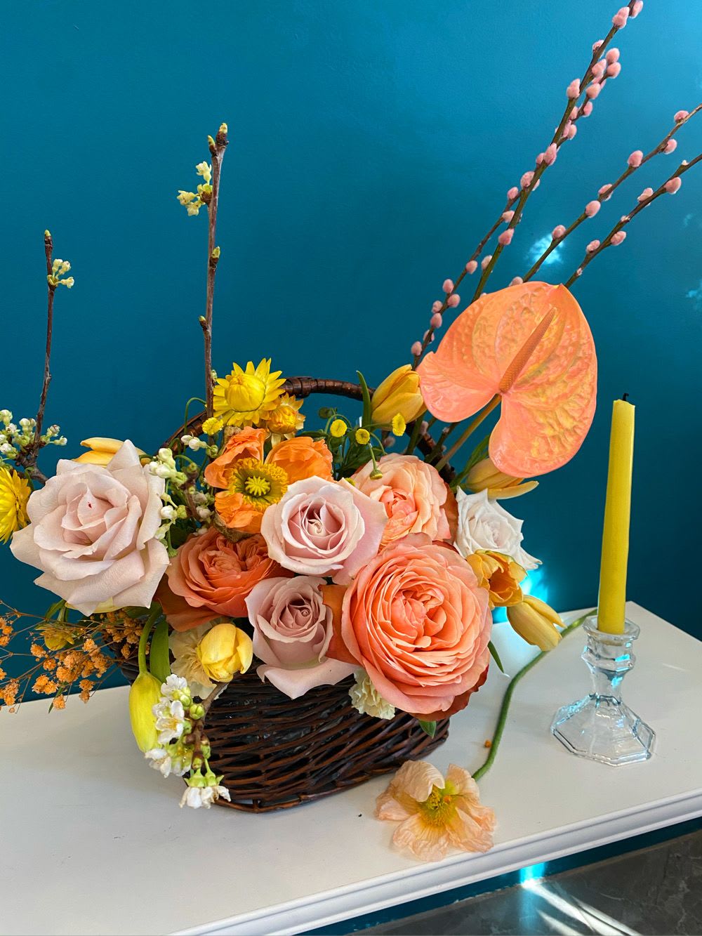 Basket arrangement of peach and pink roses with yellow accents and a candle