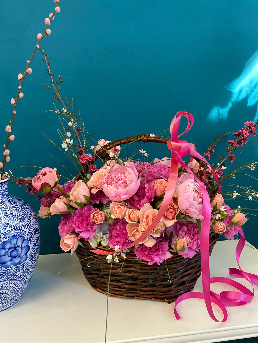 Pink and peach flowers in a wicker basket with a pink ribbon