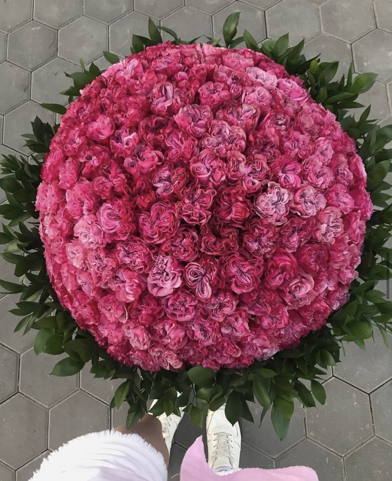Large round bouquet of pink roses with a dark green leaf border