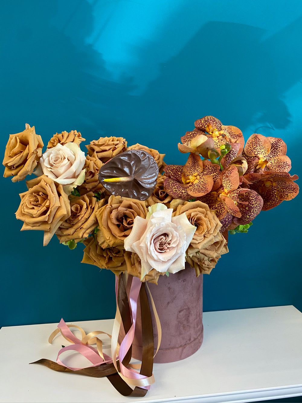 Bouquet of tan roses and spotted orchids in a velvet hatbox