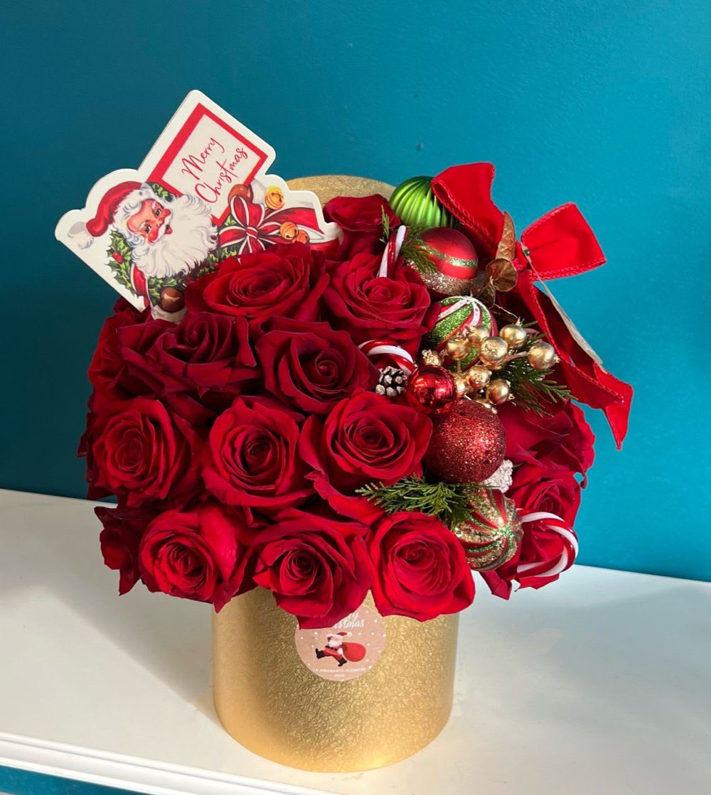 Red roses arranged in a gold box with Christmas ornaments and a Santa card