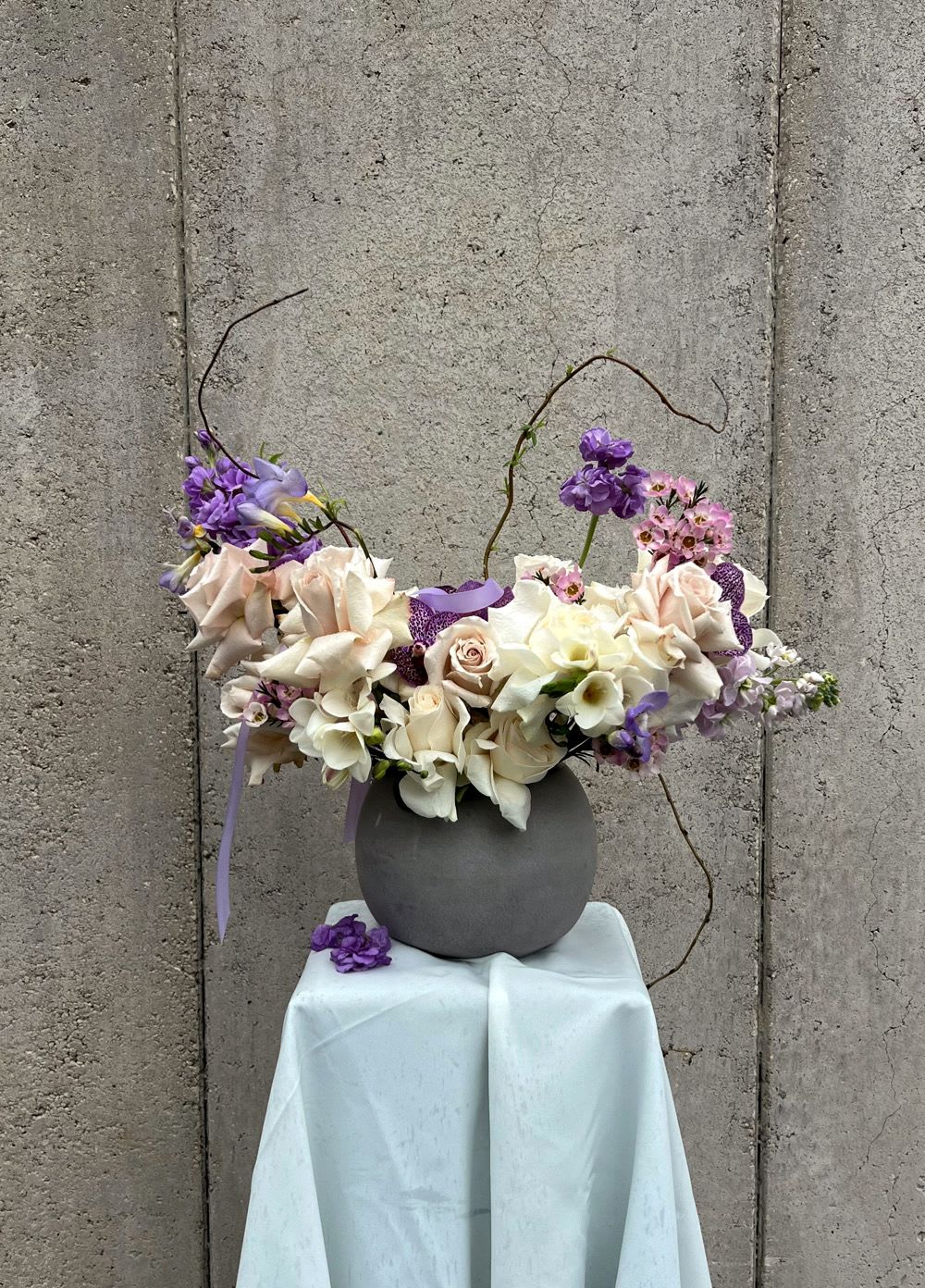 Purple and white floral arrangement in a gray vase on a draped pedestal