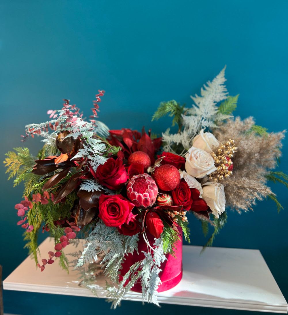 Red and white rose arrangement in a pink hat box with decorative accents