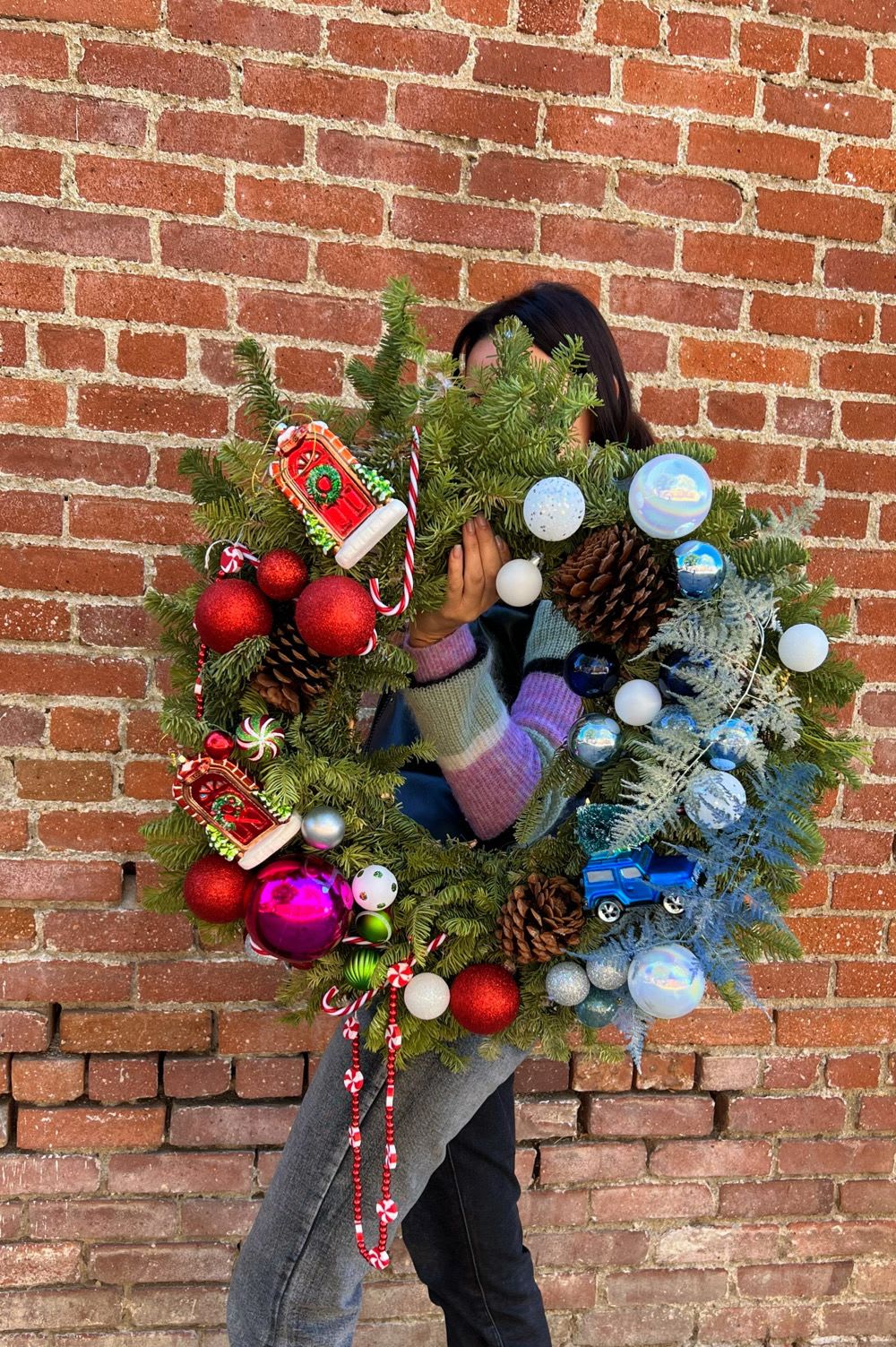 Person holding a decorated Christmas wreath with ornaments and pinecones