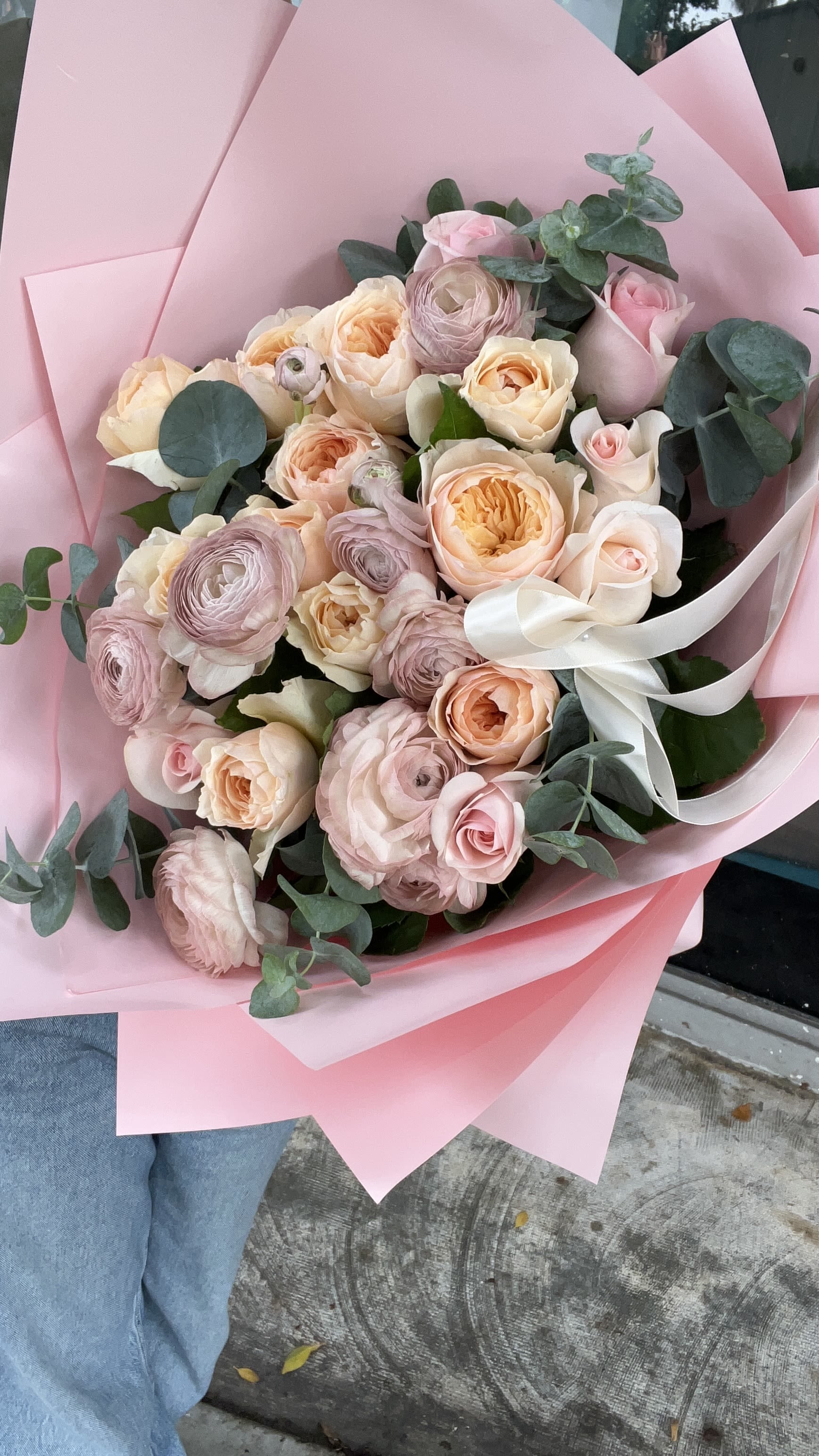 Bouquet of blush and peach roses with eucalyptus wrapped in pink paper