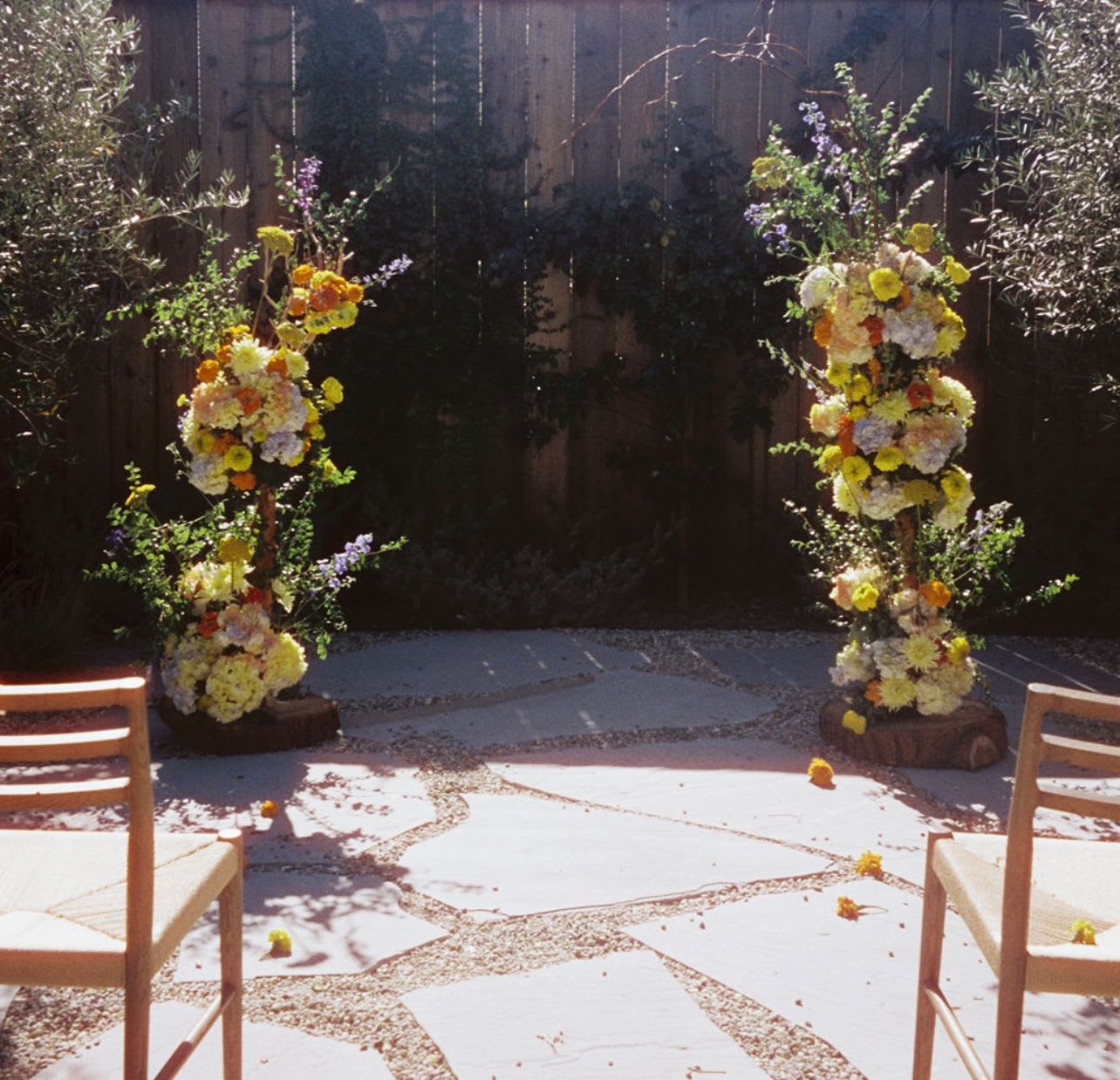 Two tall floral arrangements flank an outdoor ceremony space with chairs in front.