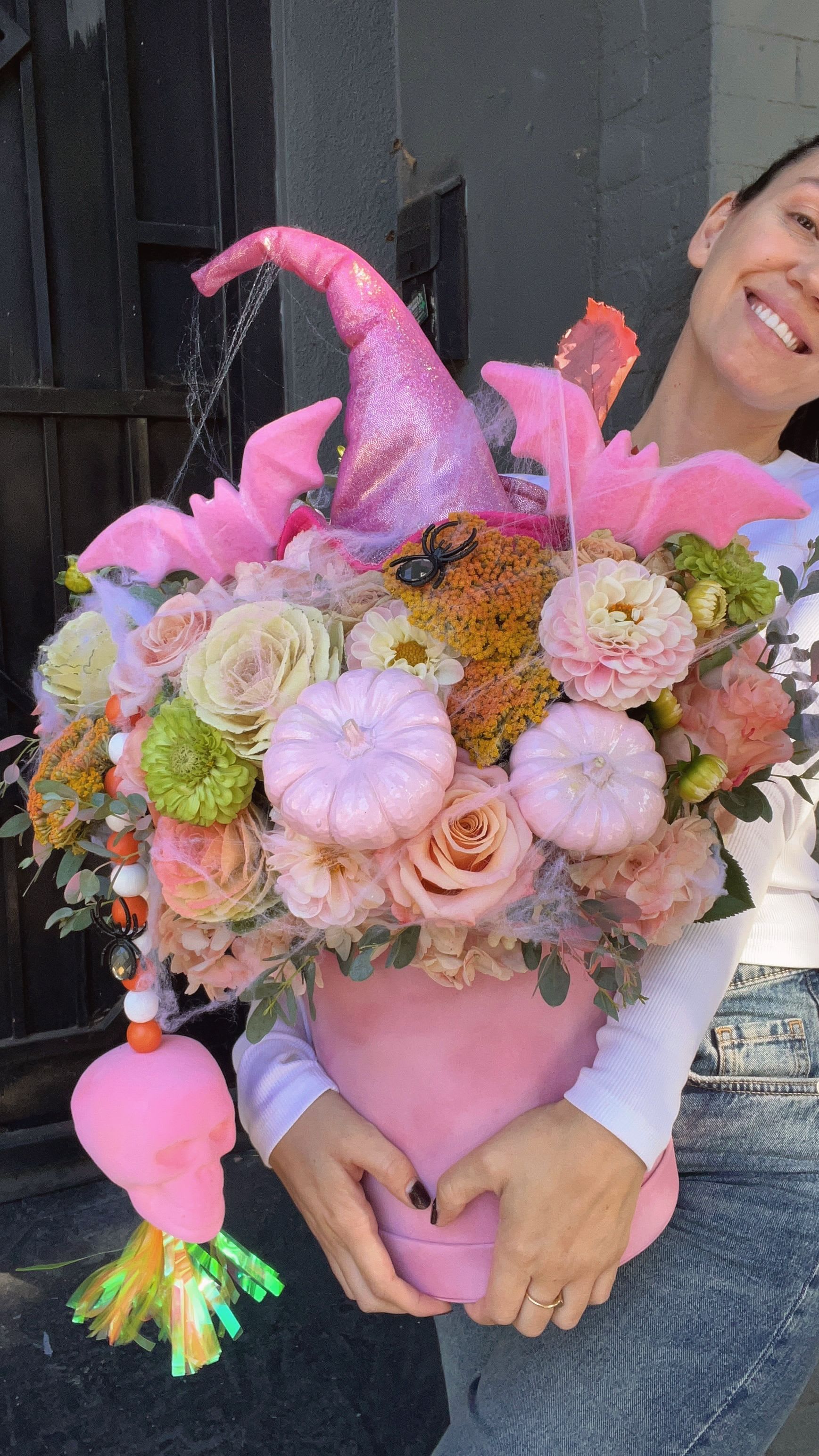 Pink pumpkin-shaped floral arrangement with roses, dahlias, and Halloween decorations