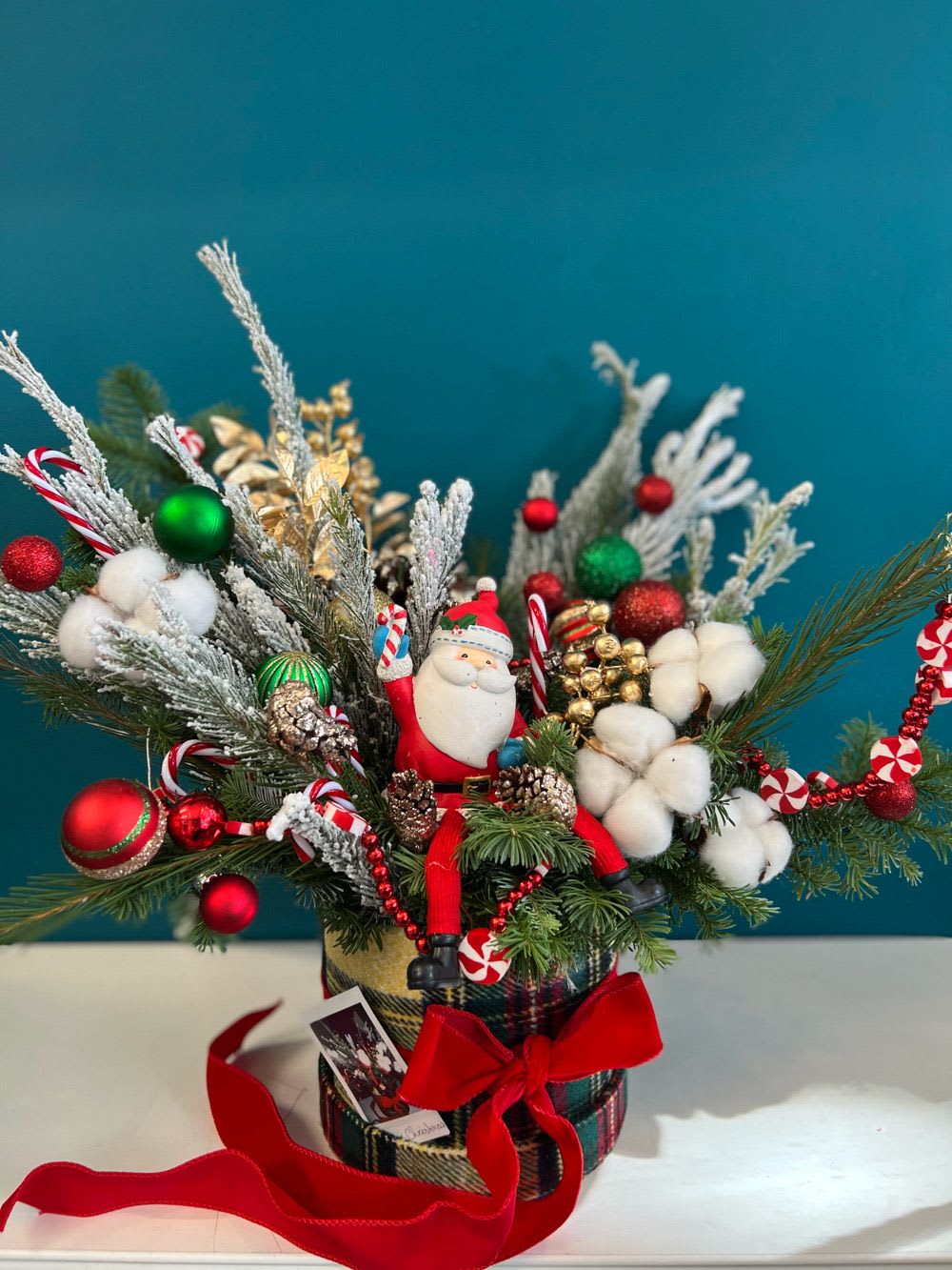 Christmas arrangement with Santa figurine, ornaments, and cotton stems in a plaid container